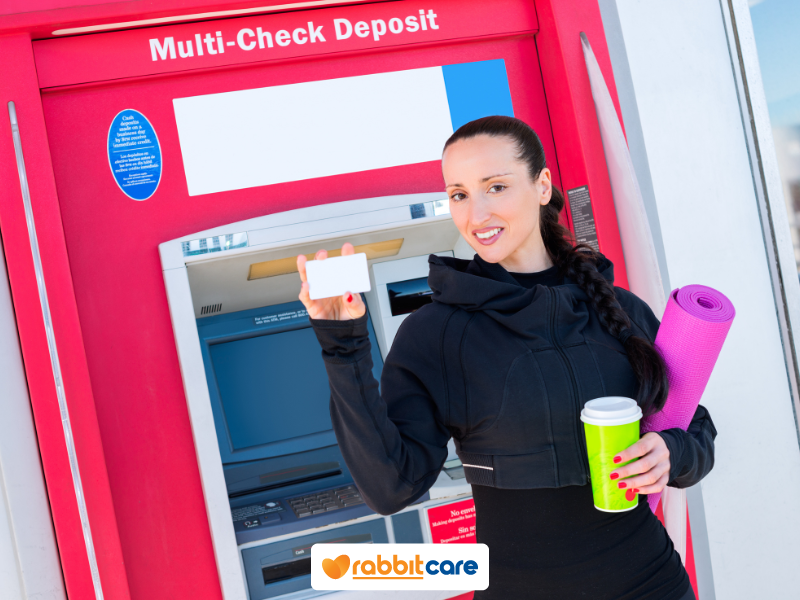 Người phụ nữ cầm thẻ ngân hàng trước cây ATM