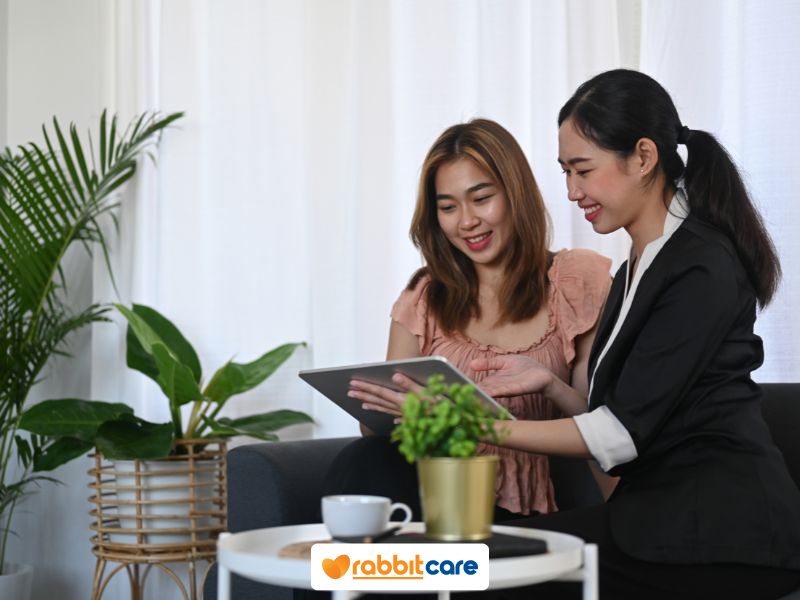Tư vấn nữ cầm ipad chỉ tay với người phụ nữ ngồi bên cạnh